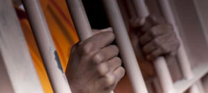hands behind cell bar representing the articles topic about Understanding California’s Revenge Porn Law