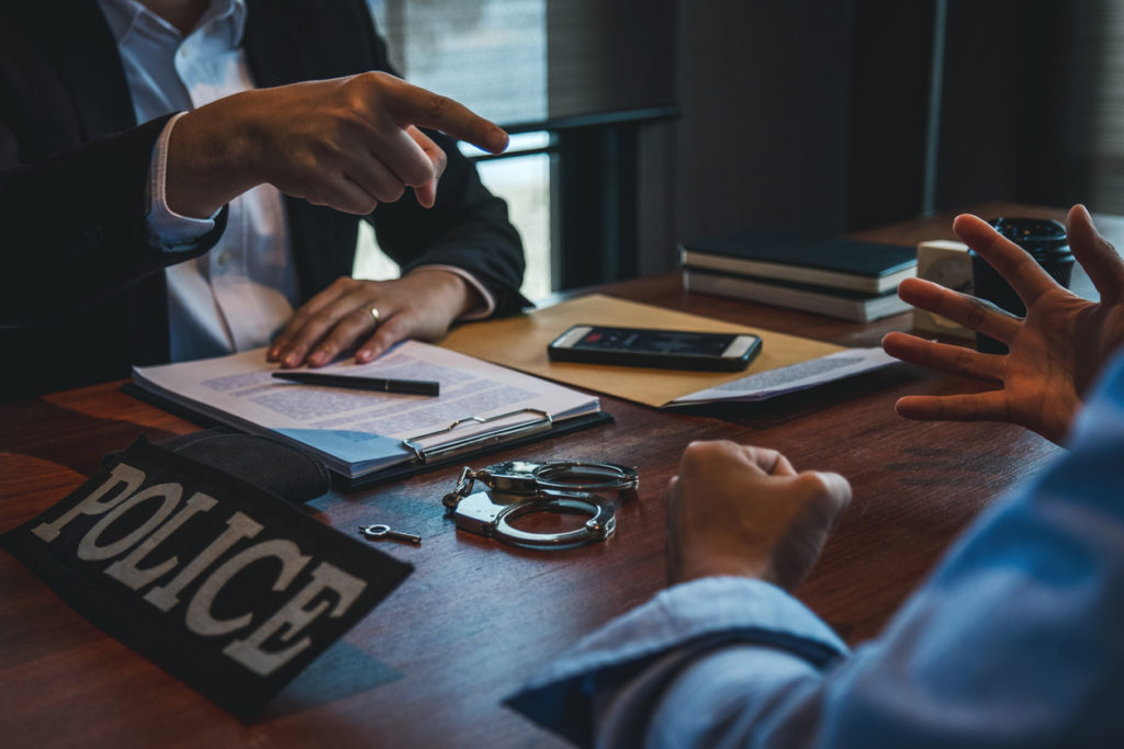 Criminal defense lawyer talking with client during police investigation with handcuffs on table.
