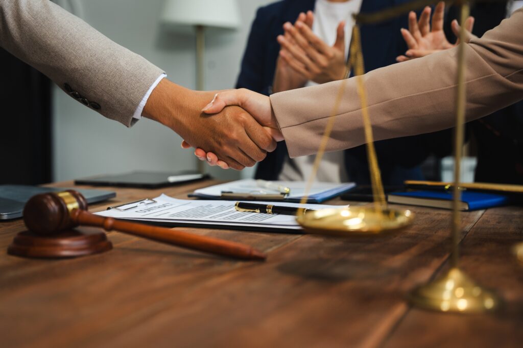 Lawyer and client shaking hands after successful legal agreement with gavel and scales of justice on desk.
