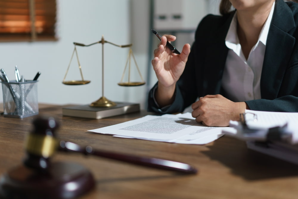Female lawyer sitting at desk with legal documents, gavel, and scales of justice during consultation.