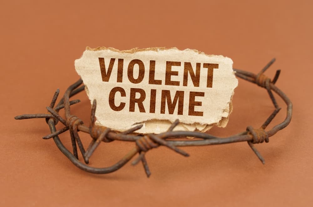 On a brown surface, barbed wire and a cardboard sign with the inscription - Violent crime