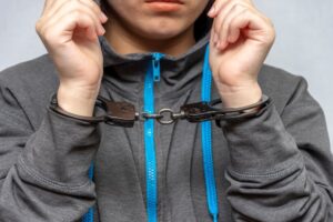 A teenage girl in handcuffs on a gray background