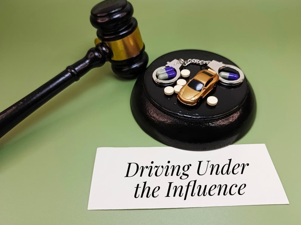 Driving Under the Influence written on paper with capsules, handcuffs, car, and judge gavel. Concept of DUI offense