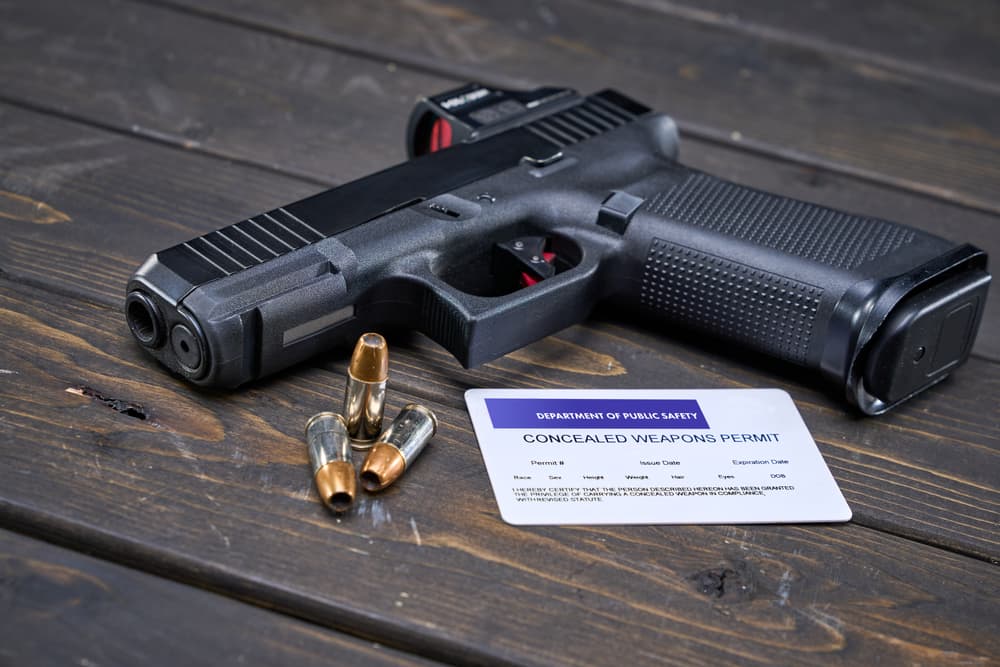 Semi-automatic handgun with 9mm self-defense ammo sitting on wood table next to concealed weapon permit