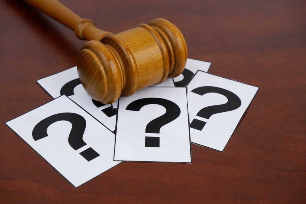 Legal FAQ concept. Wooden judge gavel and many question marks.