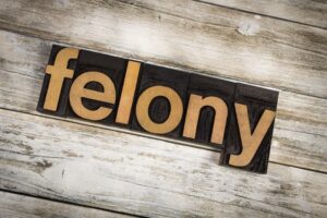 The word "felony" written in wooden letterpress type on a white washed old wooden boards background.