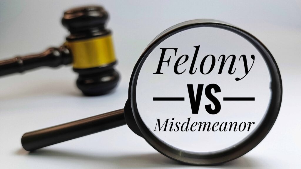 Magnifying glass highlighting the words Felony vs Misdemeanor next to a judge’s gavel.