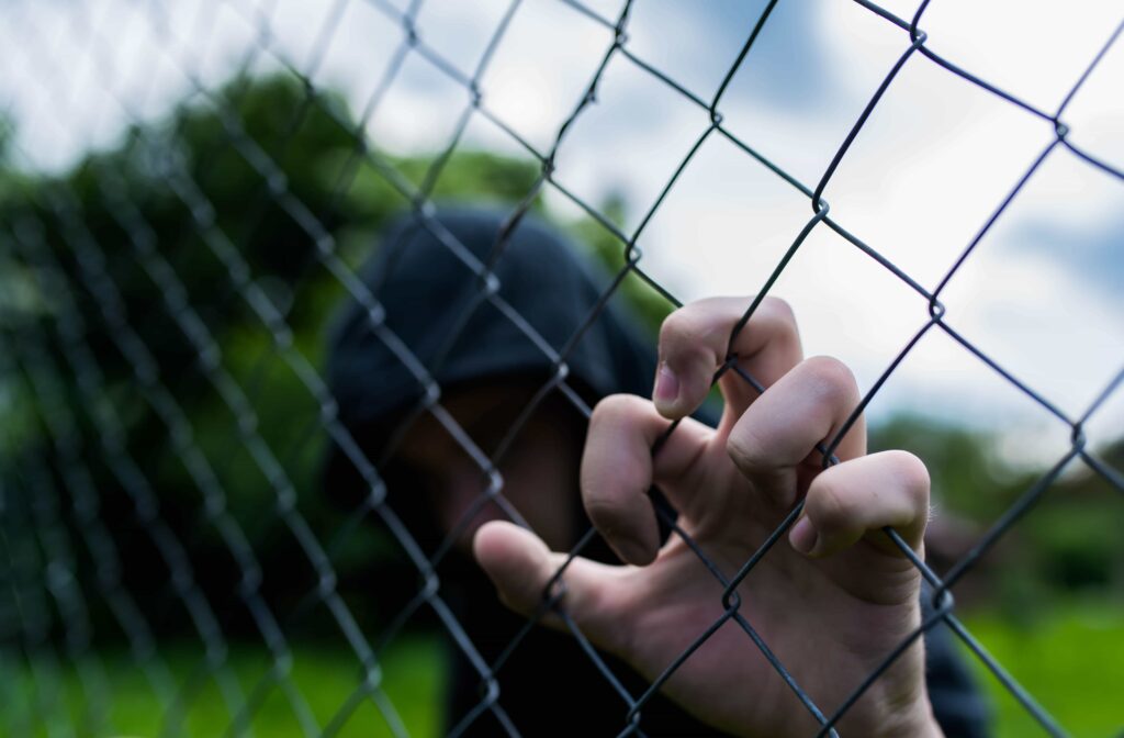 Person in hoodie gripping chain-link fence symbolizing arrest or imprisonment.