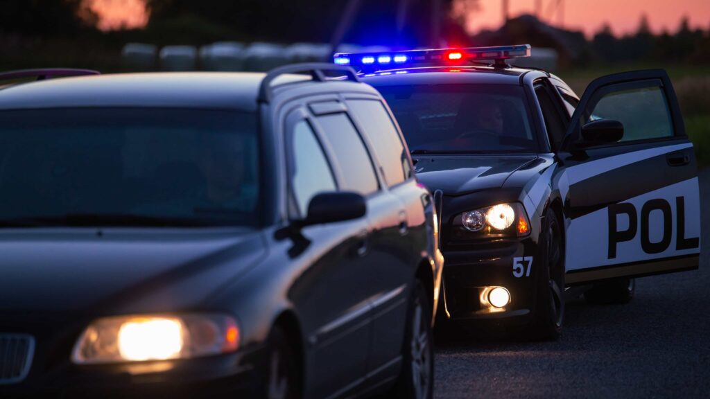 Police car with flashing lights pulling over vehicle during traffic stop at dusk.